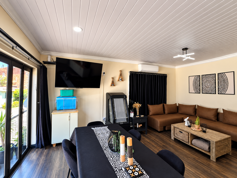Spacious open-plan living and dining area featuring laminate flooring, a tongue and groove ceiling, and direct access to the exterior through sliding glass doors.