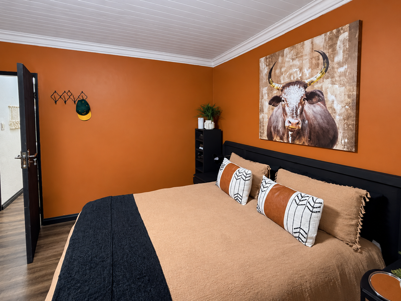 A well-maintained bedroom featuring warm orange walls, timber-look flooring, and a classic tongue and groove ceiling with crown molding.