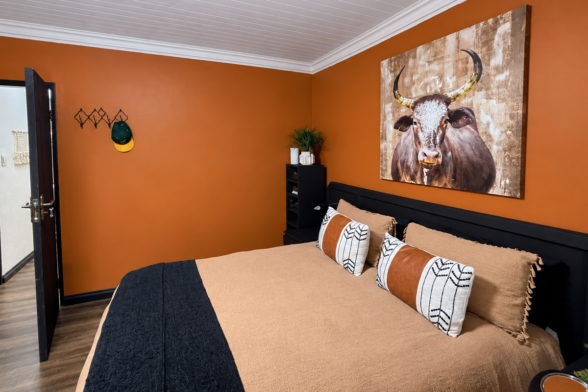 A well-maintained bedroom featuring warm orange walls, timber-look flooring, and a classic tongue and groove ceiling with crown molding.