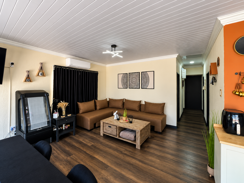 A well-maintained open-plan living area featuring modern laminate flooring, a clean tongue and groove ceiling, and a wall-mounted air conditioning unit.