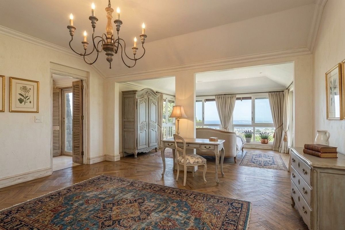 Spacious bedroom featuring elegant herringbone hardwood flooring, crown molding, and large windows offering scenic views, complemented by a classic chandelier.