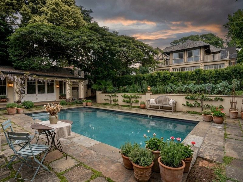 A beautifully landscaped pool area featuring stone paving, a well-maintained swimming pool, and a charming retaining wall with integrated outdoor lighting.