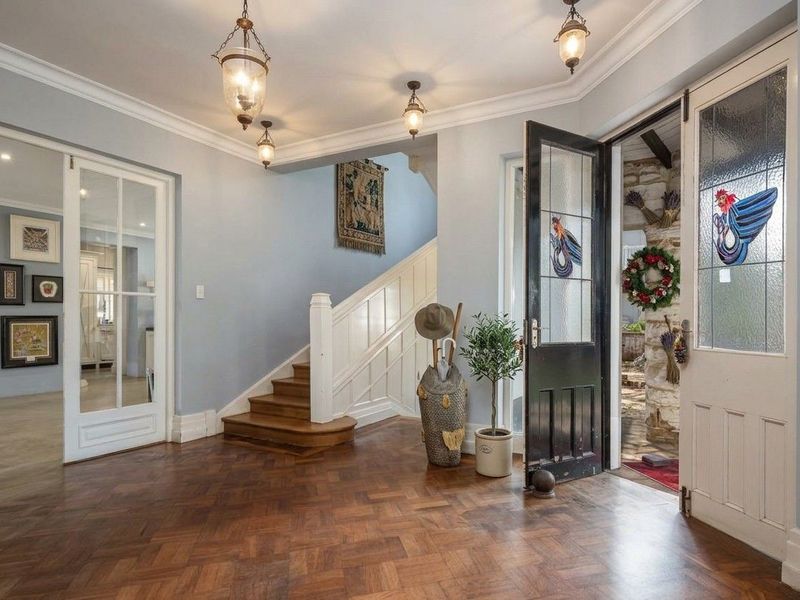 Welcoming entrance hall featuring classic herringbone parquet flooring, a timber staircase, and elegant leaded glass front doors with traditional architectural detailing.