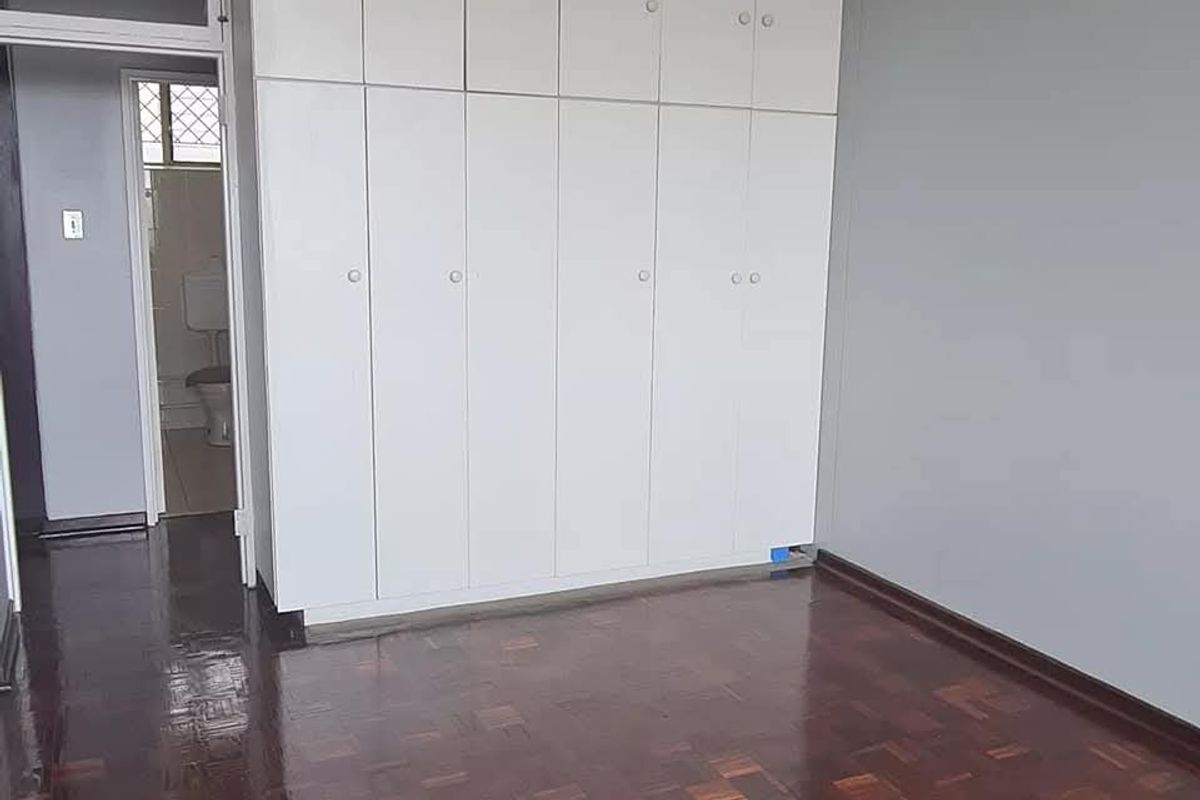 A clean, empty bedroom featuring polished parquet flooring and extensive floor-to-ceiling built-in cupboards, with direct access to an adjacent bathroom.