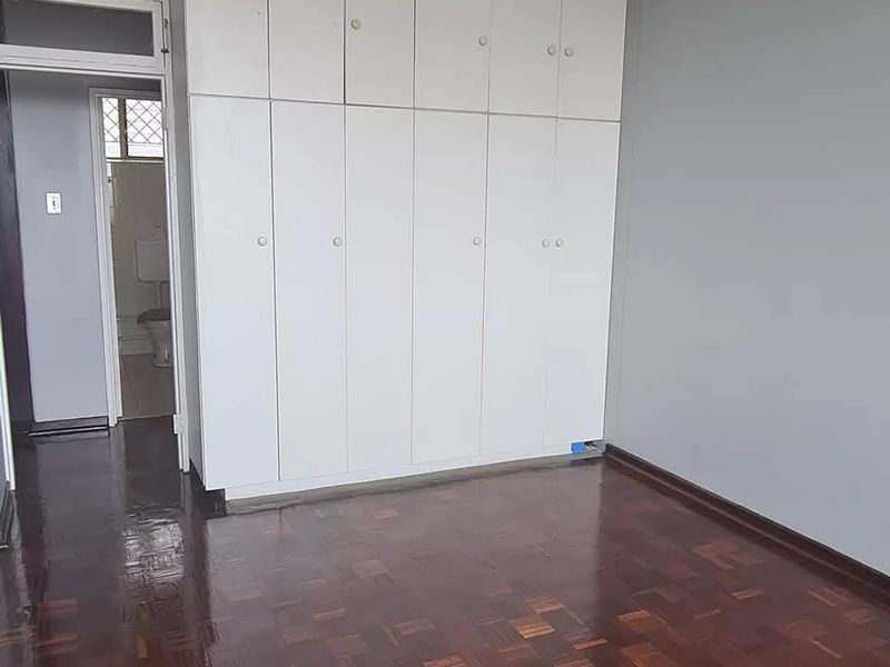 A clean, empty bedroom featuring polished parquet flooring and extensive floor-to-ceiling built-in cupboards, with direct access to an adjacent bathroom.