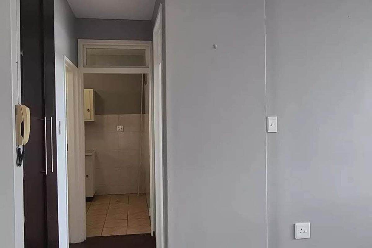 A clean hallway featuring parquet flooring, built-in storage, and an intercom system, leading through to a tiled utility or kitchen area.