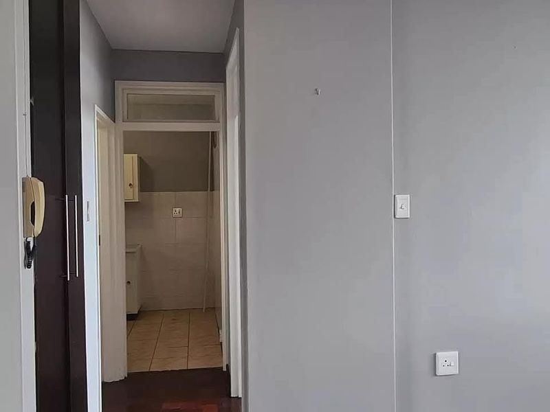 A clean hallway featuring parquet flooring, built-in storage, and an intercom system, leading through to a tiled utility or kitchen area.
