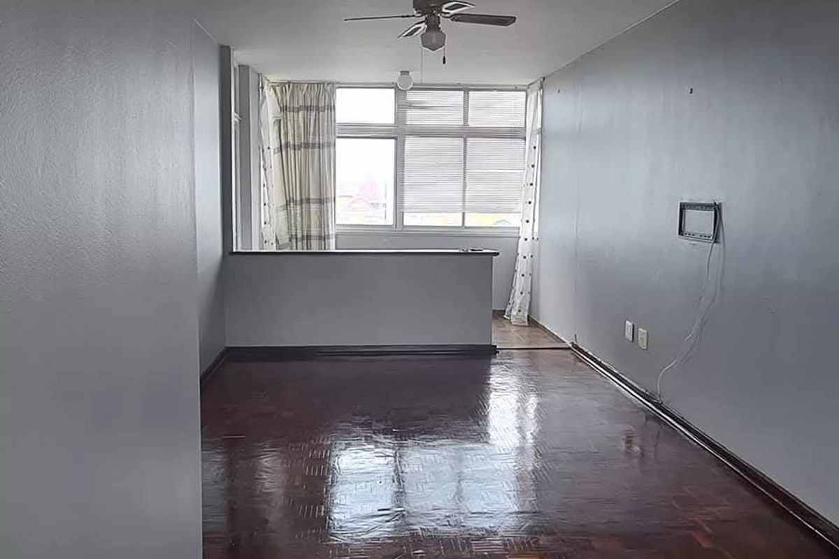 Spacious living area featuring polished parquet flooring, a ceiling fan, and a half-height partition wall, offering a bright and open layout.