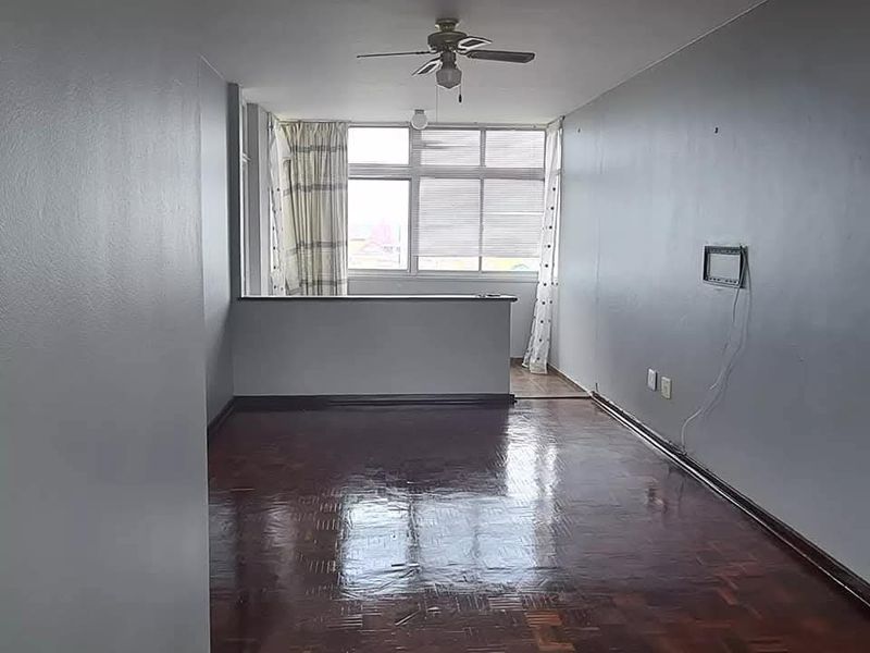 Spacious living area featuring polished parquet flooring, a ceiling fan, and a half-height partition wall, offering a bright and open layout.