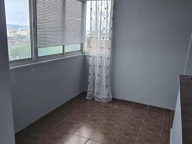 An empty, enclosed balcony area featuring tiled flooring and large windows with venetian blinds, offering an elevated view of the surrounding area.