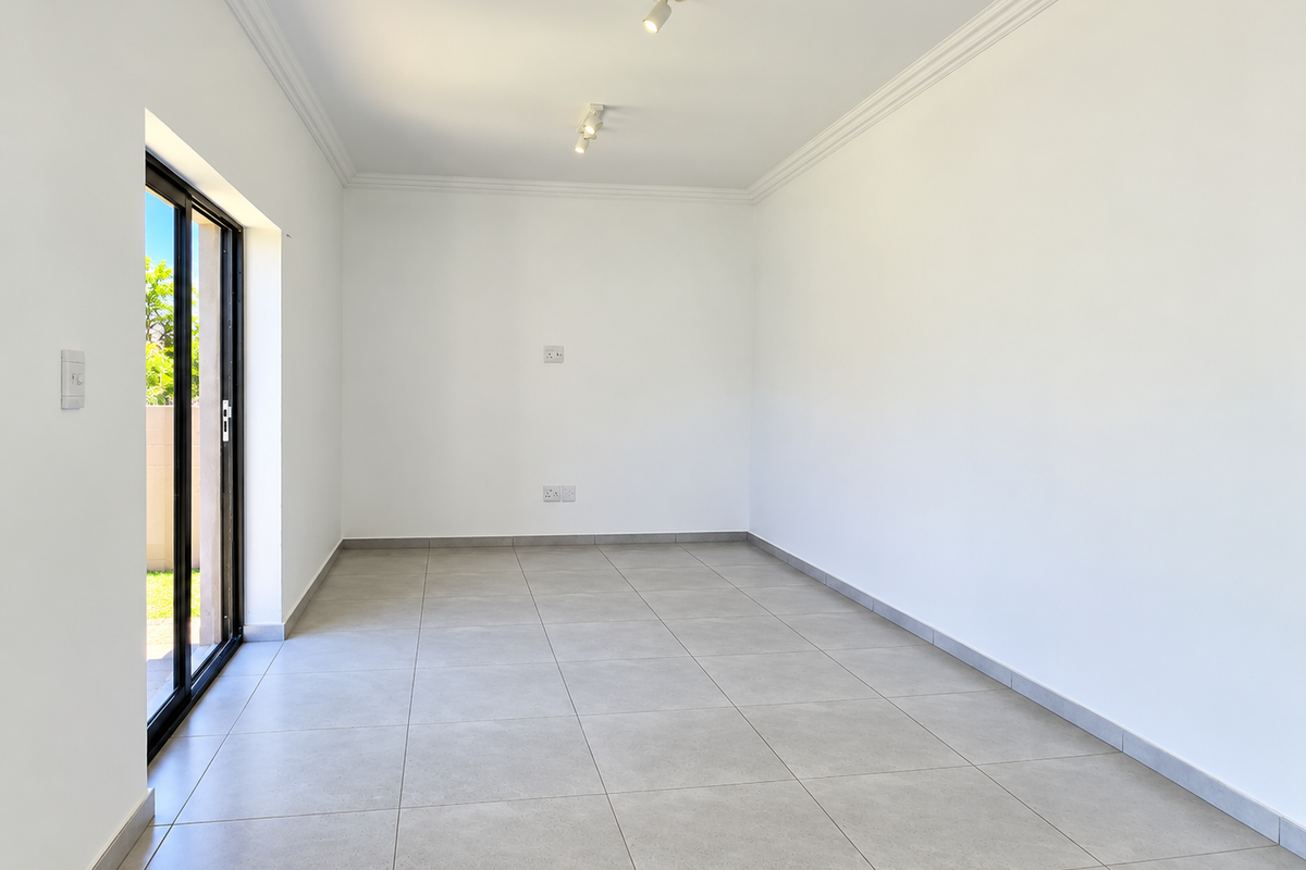 A bright, empty living room featuring neutral tiled flooring, coved cornicing, and a sliding glass door providing direct access to the outdoor area.