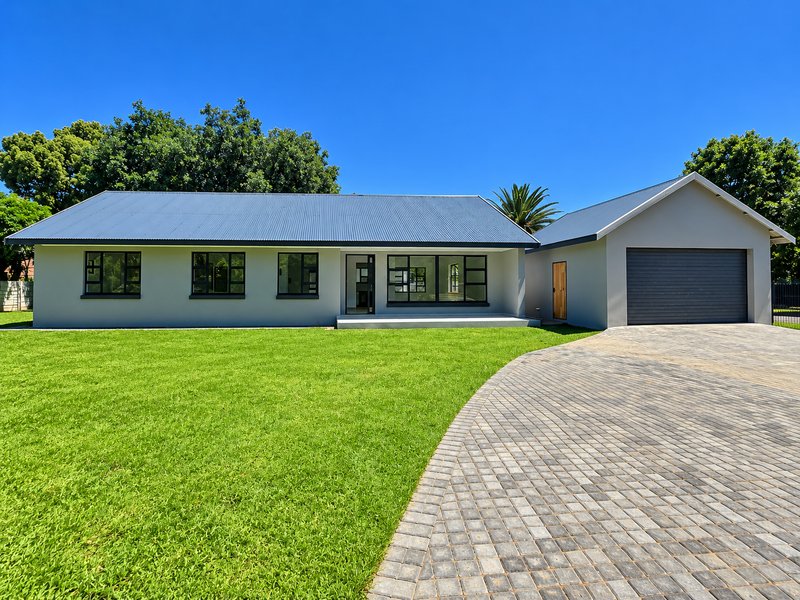 A well-maintained single-story home featuring a modern grey facade, corrugated metal roof, paved driveway, and a spacious front lawn.