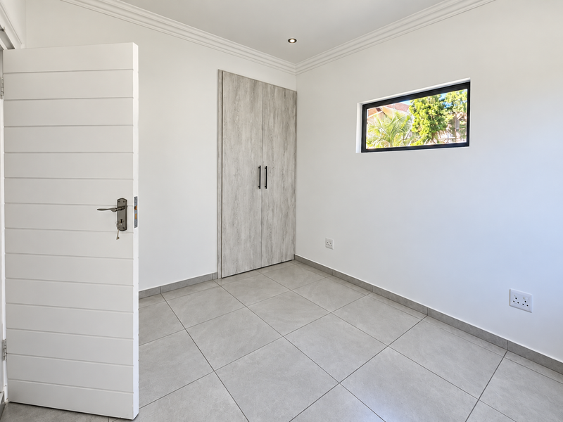 A bright, empty bedroom featuring modern grey tiled flooring, a built-in wardrobe with wood-grain finish, and a horizontal slat door.