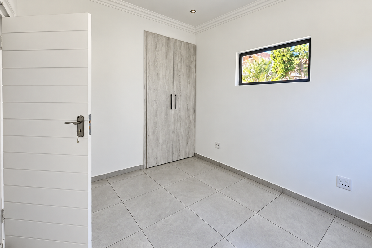 A bright, empty bedroom featuring modern grey tiled flooring, a built-in wardrobe with wood-grain finish, and a horizontal slat door.