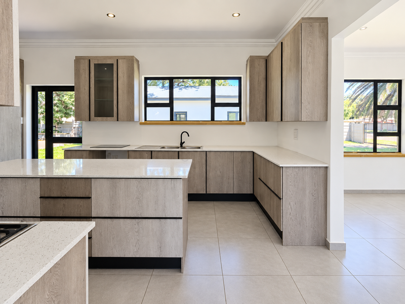 Modern kitchen featuring light wood-grain cabinetry, quartz countertops, a central island, and large windows providing ample natural light.