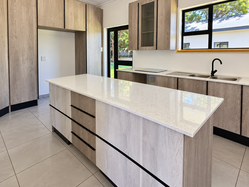 Modern kitchen featuring light wood-grain cabinetry, white quartz countertops, a central island, and sleek black fixtures, offering a clean and contemporary aesthetic.