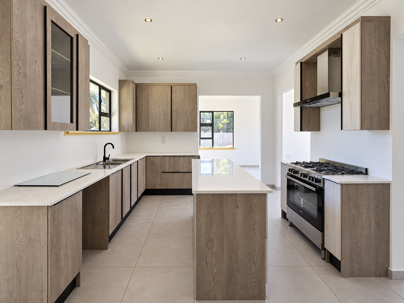 Modern kitchen featuring wood-finish cabinetry, stone countertops, a central island, and high-quality built-in appliances including a gas hob and oven.