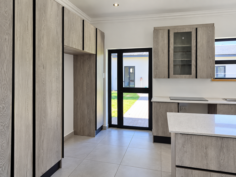 Modern kitchen featuring light wood-grain cabinetry, stone countertops, integrated hob, and tiled flooring with direct access to the rear garden.