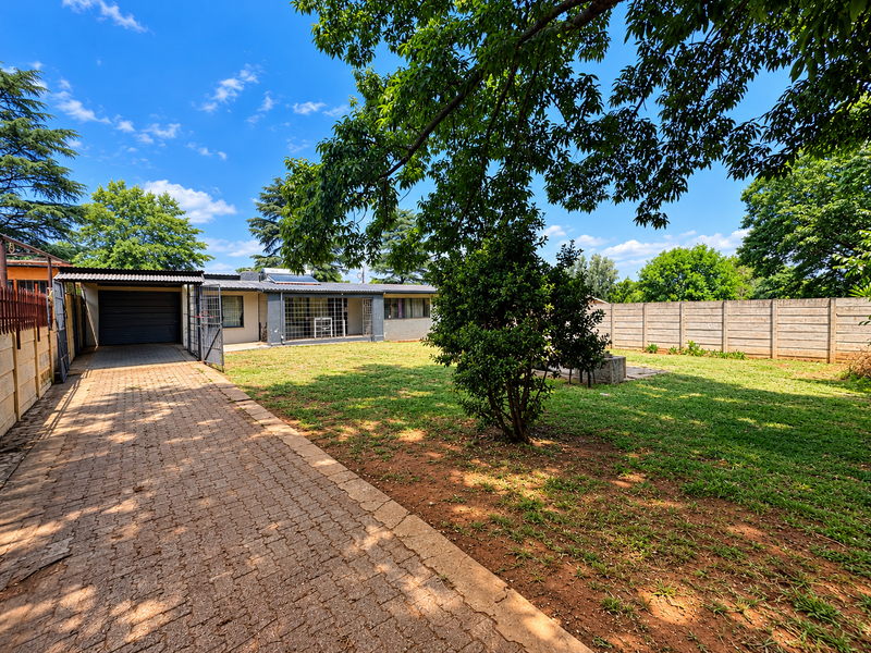 Spacious rear garden featuring a paved driveway leading to a single garage, enclosed by a precast concrete boundary wall.