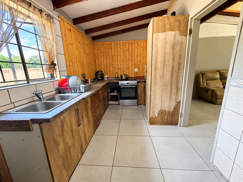 A kitchen featuring wooden cabinetry, exposed timber ceiling beams, tiled flooring, and a freestanding stove, requiring cosmetic updates to improve the overall finish.