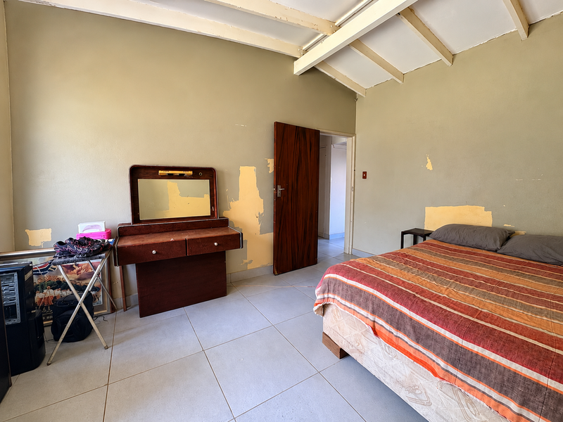 A bedroom featuring tiled flooring and exposed ceiling beams, currently requiring wall repairs and repainting to restore the space.