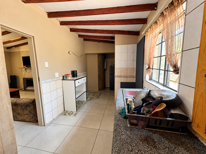 A functional kitchen area featuring exposed timber ceiling beams, tiled splashbacks, and a granite-look countertop, offering potential for a modern renovation.
