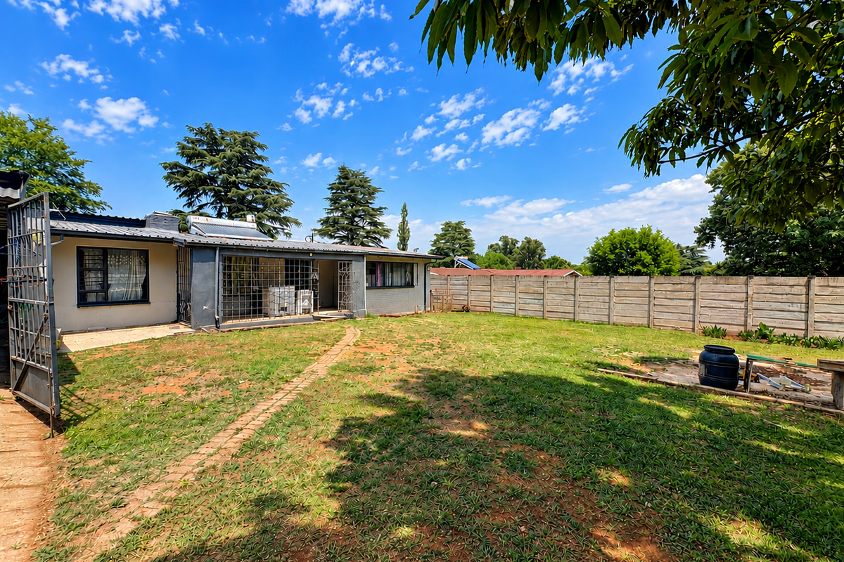 Rear view of the property featuring a spacious garden, paved walkway, security bars on windows, and a solar water heating system.