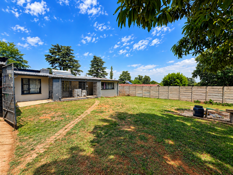 Rear view of the property featuring a spacious garden, paved walkway, security bars on windows, and a solar water heating system.