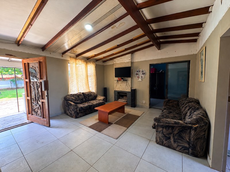 Spacious living room featuring exposed timber ceiling beams, a brick fireplace, and tiled flooring, with direct access to the outdoor area.