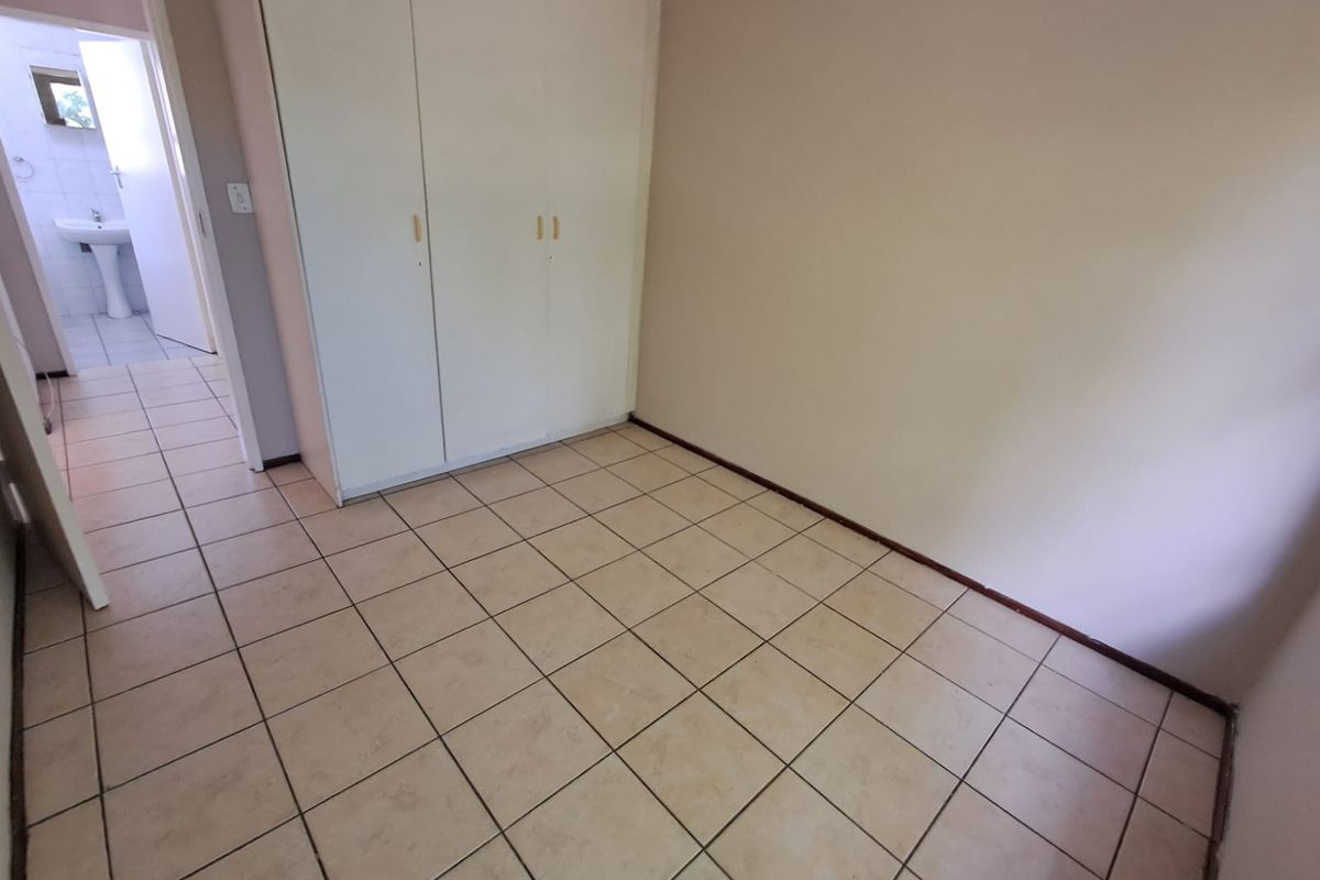 An empty bedroom featuring tiled flooring and built-in cupboards, with an adjacent view into a bathroom area.