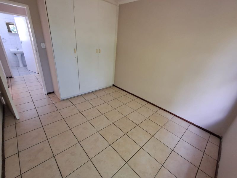 An empty bedroom featuring tiled flooring and built-in cupboards, with an adjacent view into a bathroom area.