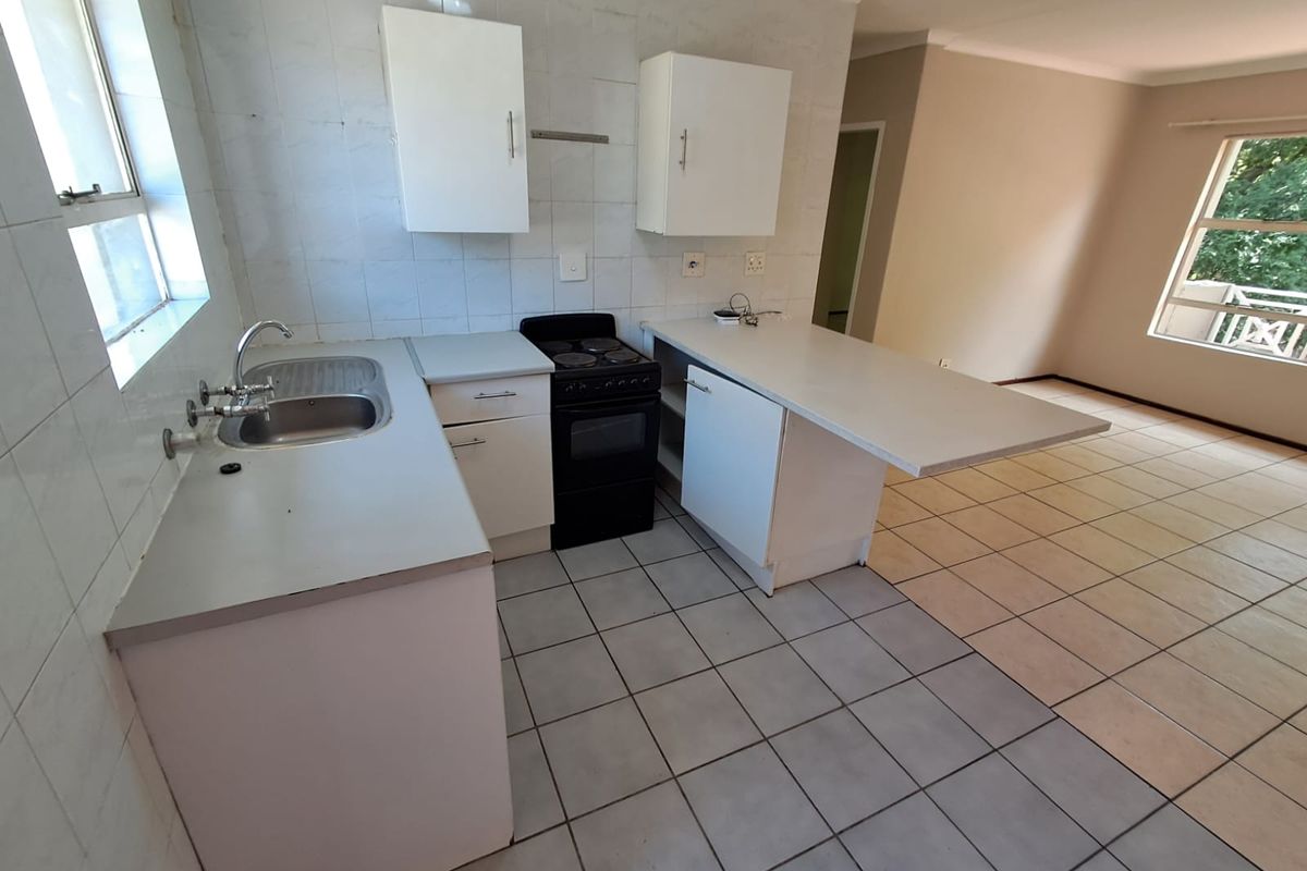 An open-plan kitchen and living area featuring tiled flooring, built-in cabinetry, and a functional layout, presenting a blank canvas for renovation.