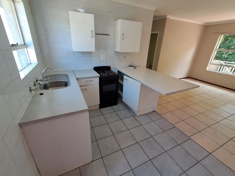 An open-plan kitchen and living area featuring tiled flooring, built-in cabinetry, and a functional layout, presenting a blank canvas for renovation.