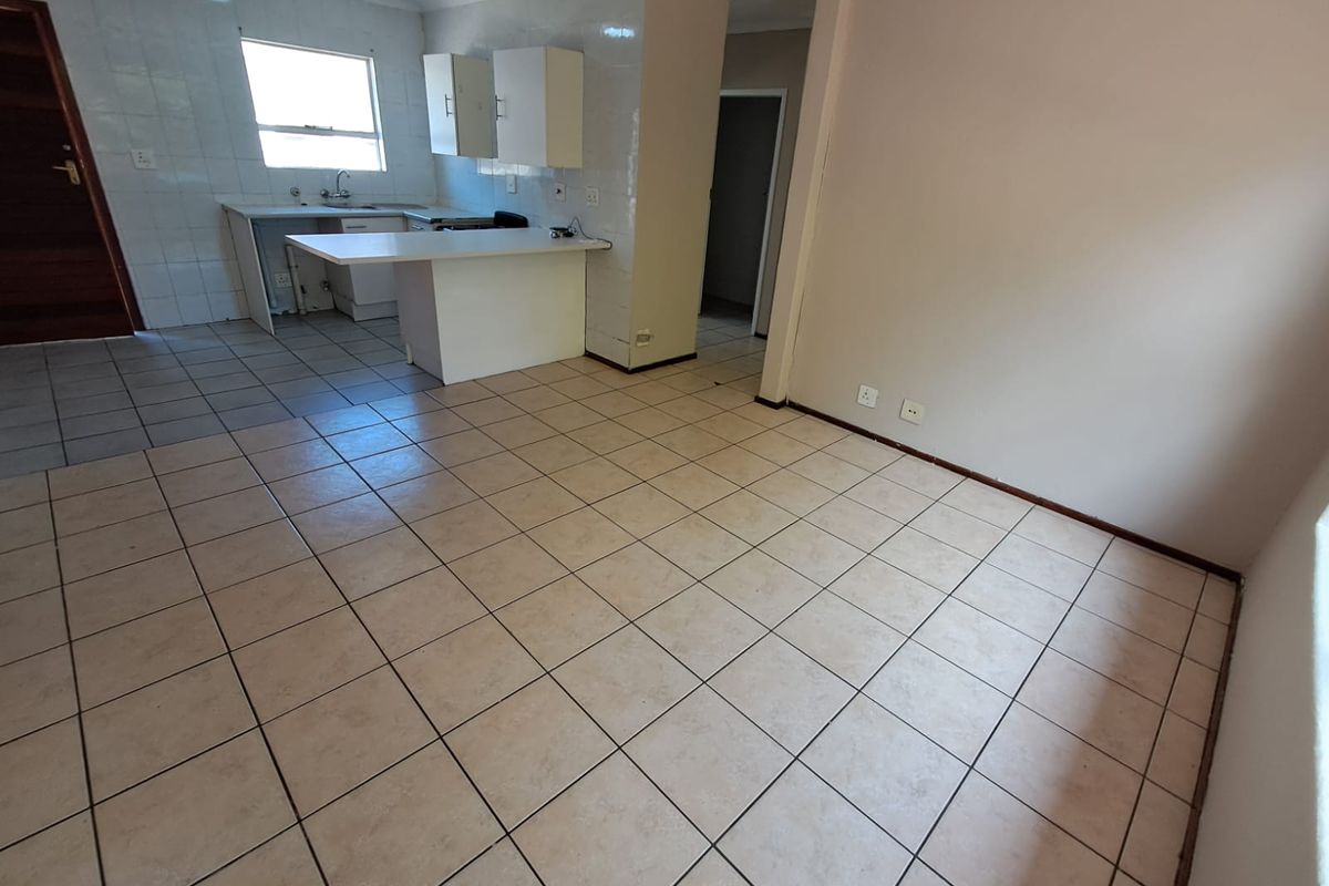 An open-plan living and kitchen area featuring tiled flooring, a breakfast counter, and functional kitchen cabinetry.