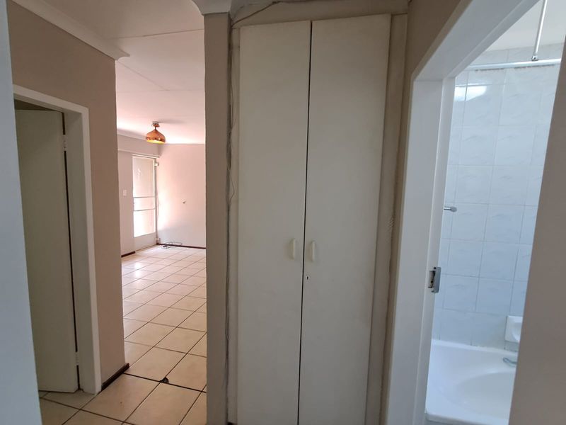 A hallway featuring tiled flooring, a built-in storage cupboard, and access to adjacent living and bathroom areas.