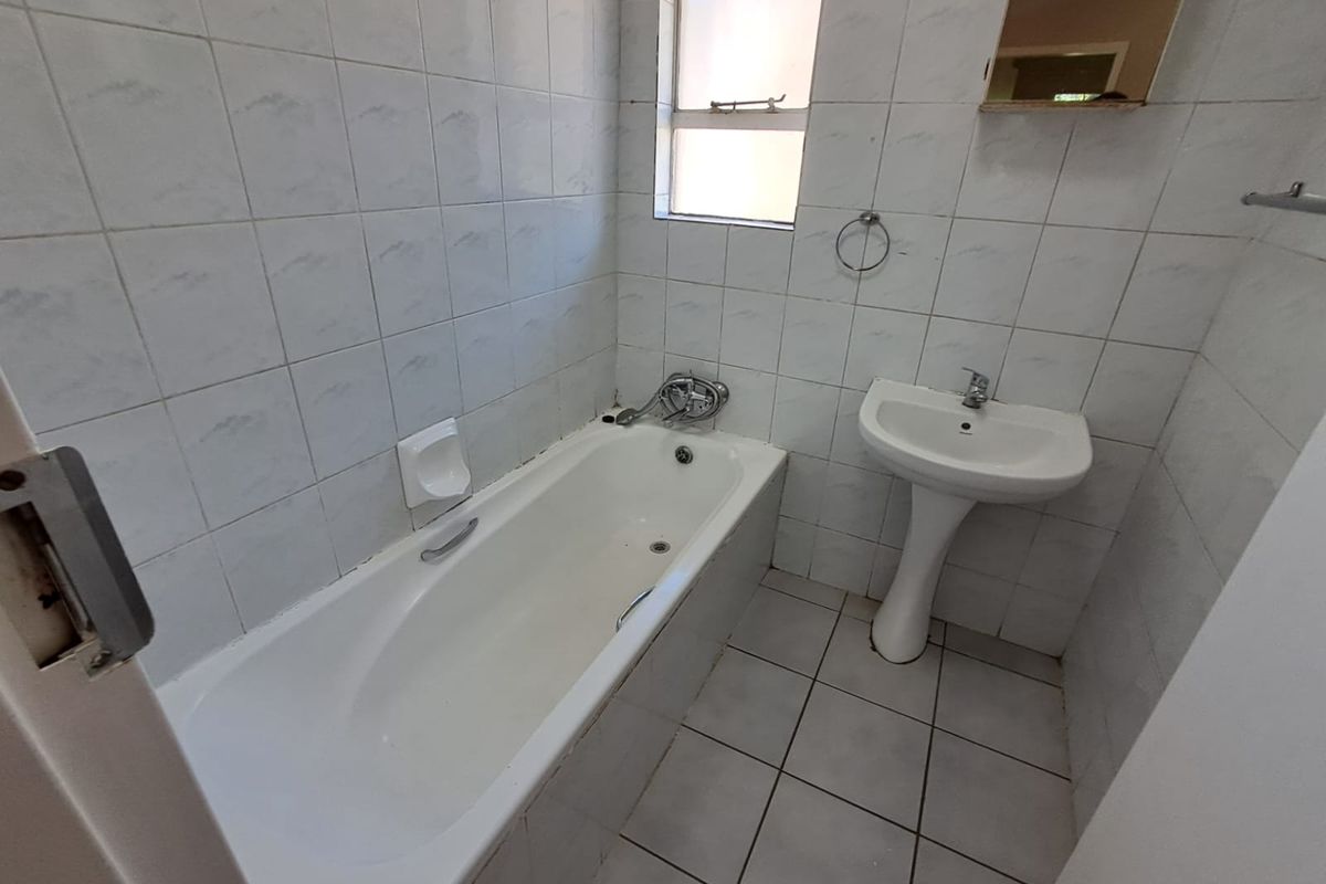 A compact bathroom featuring a standard bathtub, pedestal basin, and full-height wall tiling. The space is functional but would benefit from modern updates.