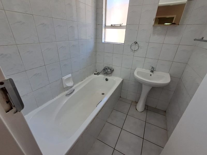 A compact bathroom featuring a standard bathtub, pedestal basin, and full-height wall tiling. The space is functional but would benefit from modern updates.