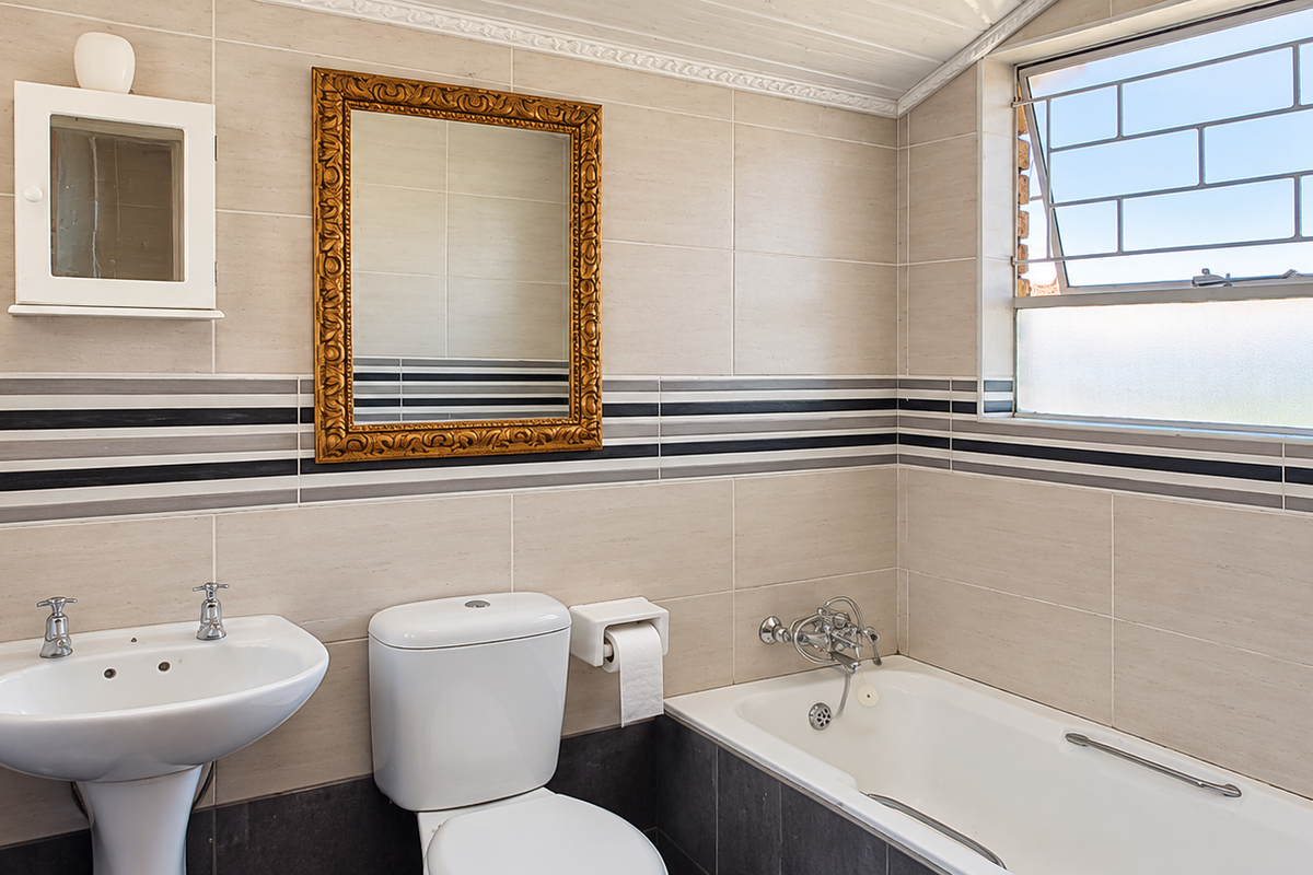 A functional bathroom featuring a pedestal basin, toilet, and bathtub with tiled walls and flooring, offering a clean and practical layout.