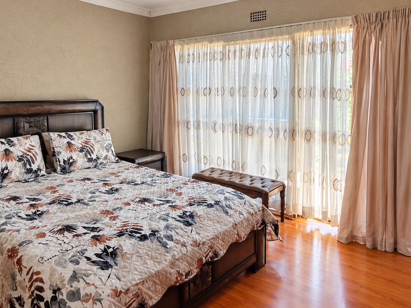 Spacious bedroom featuring laminate flooring, large sliding glass doors with natural light, and an adjoining en-suite bathroom with a pedestal basin and toilet.