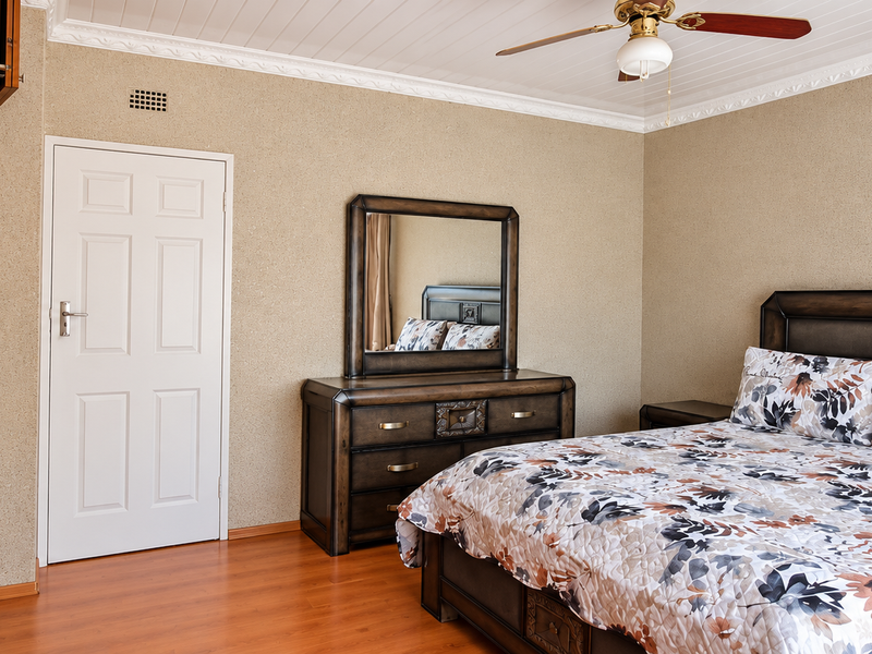 A well-maintained bedroom featuring built-in wooden cupboards, laminate flooring, and a ceiling fan, offering a comfortable and functional living space.