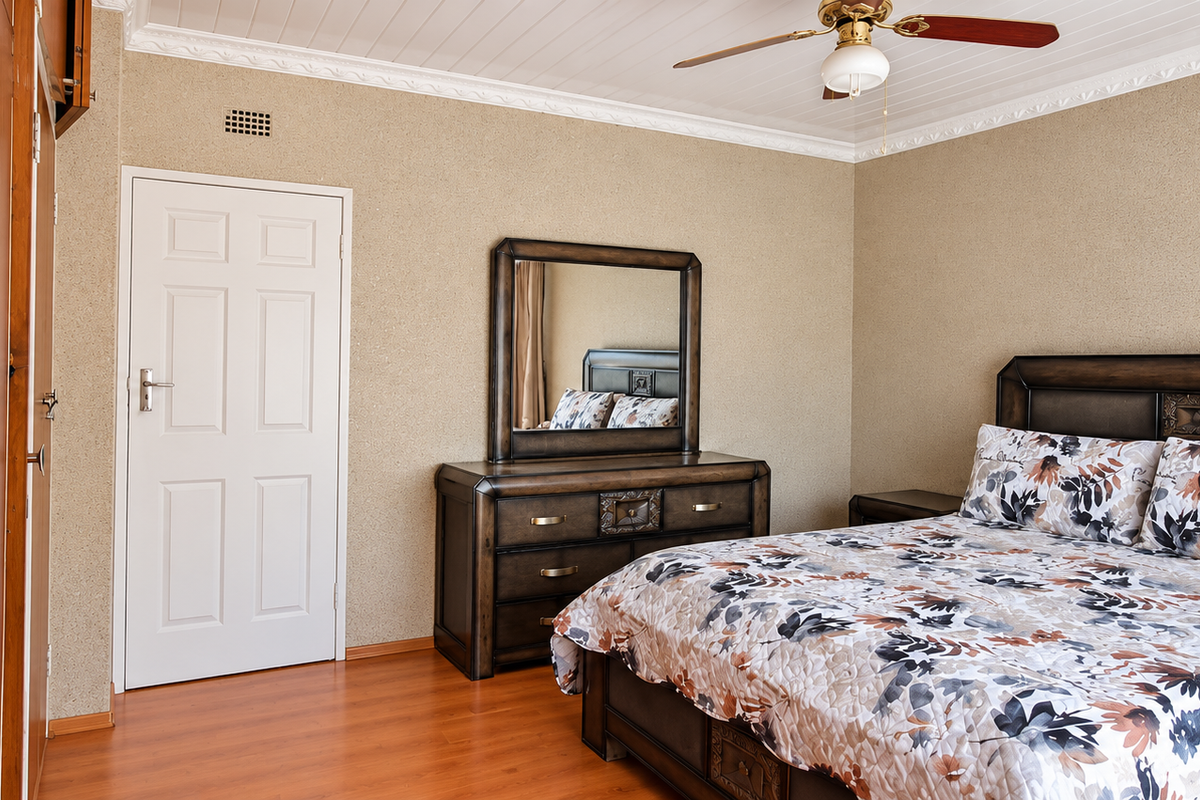 A well-maintained bedroom featuring built-in wooden cupboards, laminate flooring, and a ceiling fan, offering a comfortable and functional living space.