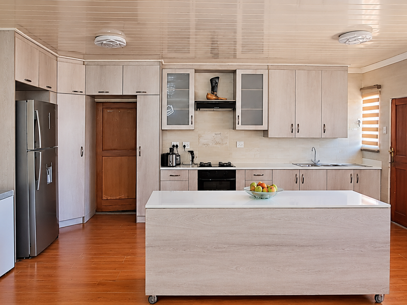 A functional kitchen featuring light wood-finish cabinetry, a central island, laminate flooring, and integrated appliances, offering a clean and practical cooking space.