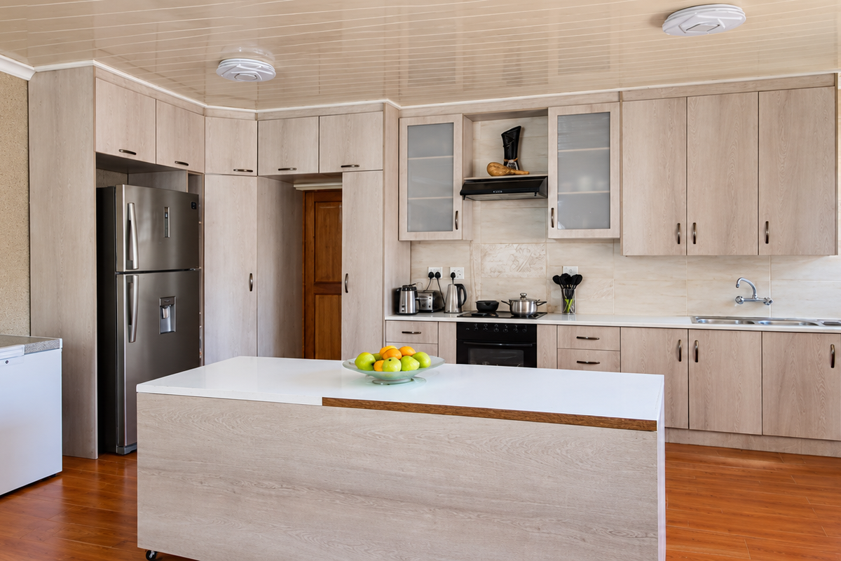 A functional kitchen featuring light wood-toned cabinetry, a central island, built-in oven with extractor fan, and a double sink with tiled backsplash.