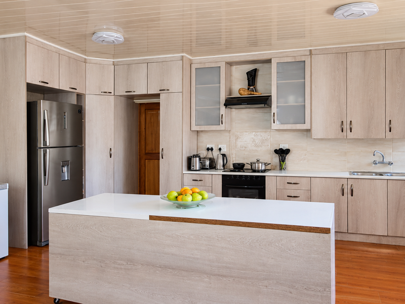 A functional kitchen featuring light wood-toned cabinetry, a central island, built-in oven with extractor fan, and a double sink with tiled backsplash.