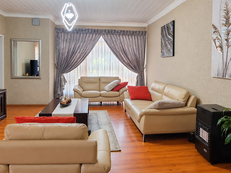 A spacious living room featuring warm-toned laminate flooring, coved ceiling detailing, and a built-in gas heater, offering a comfortable and inviting atmosphere.