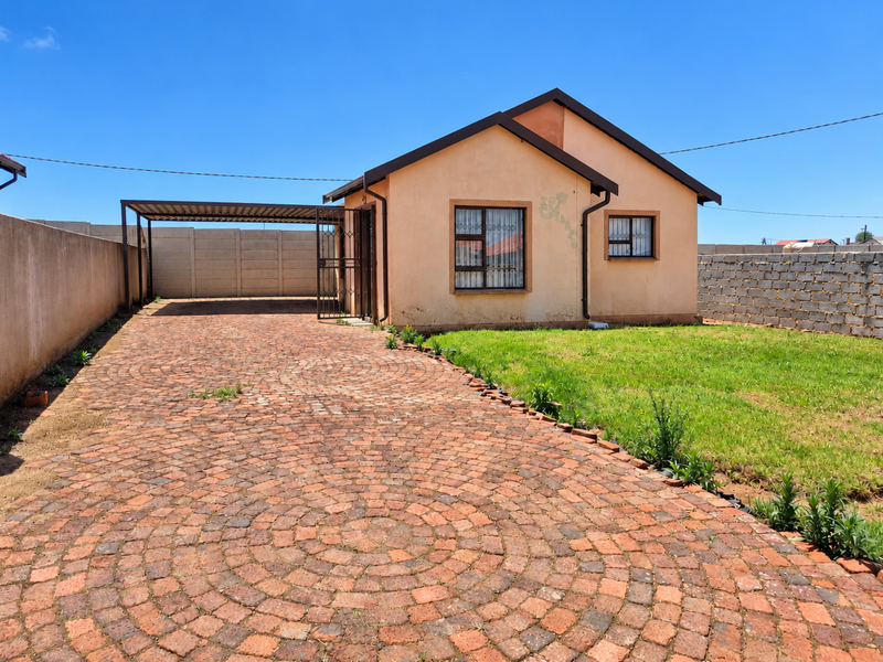A detached single-story house featuring a paved circular driveway, an attached carport, and enclosed garden space with precast and brick boundary walls.