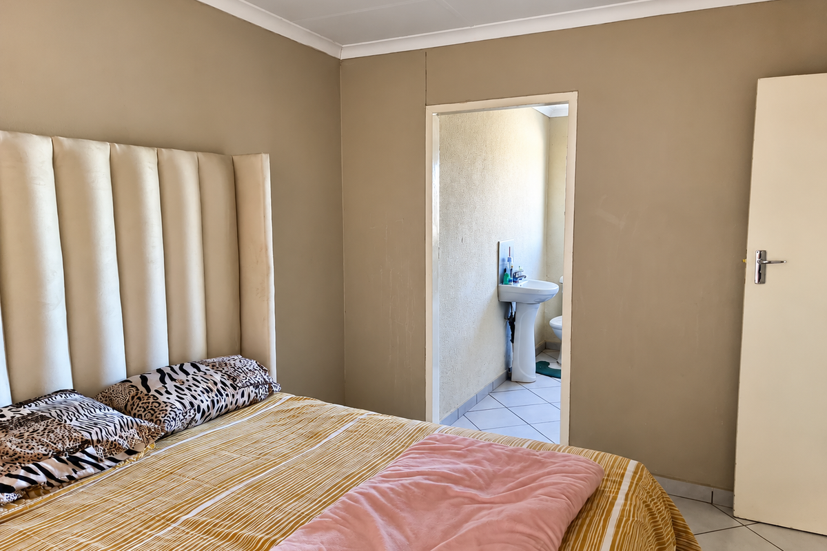 Bedroom featuring neutral wall tones and an en-suite bathroom with a pedestal basin and tiled flooring.