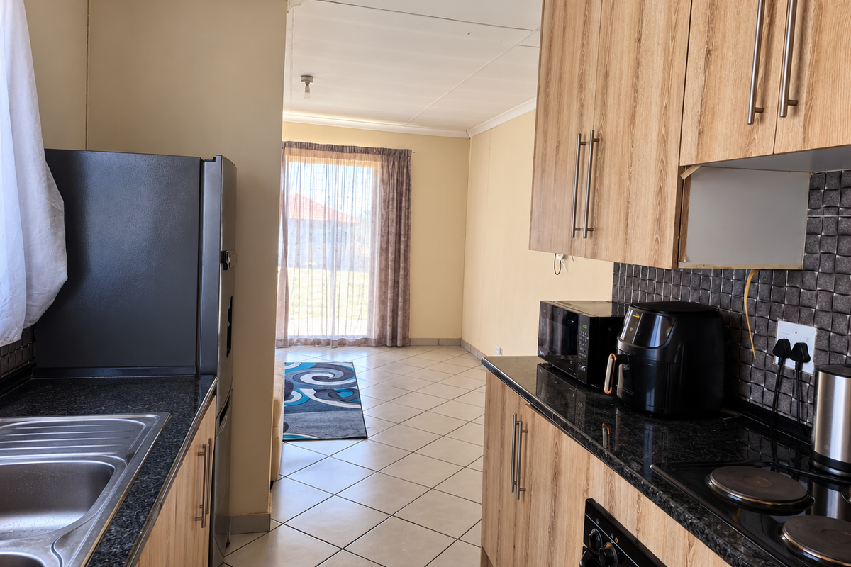 A functional kitchen featuring wood-look cabinetry, granite countertops, tiled backsplash, and integrated appliances, leading into an open-plan living area.