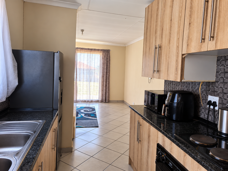 A functional kitchen featuring wood-look cabinetry, granite countertops, tiled backsplash, and integrated appliances, leading into an open-plan living area.