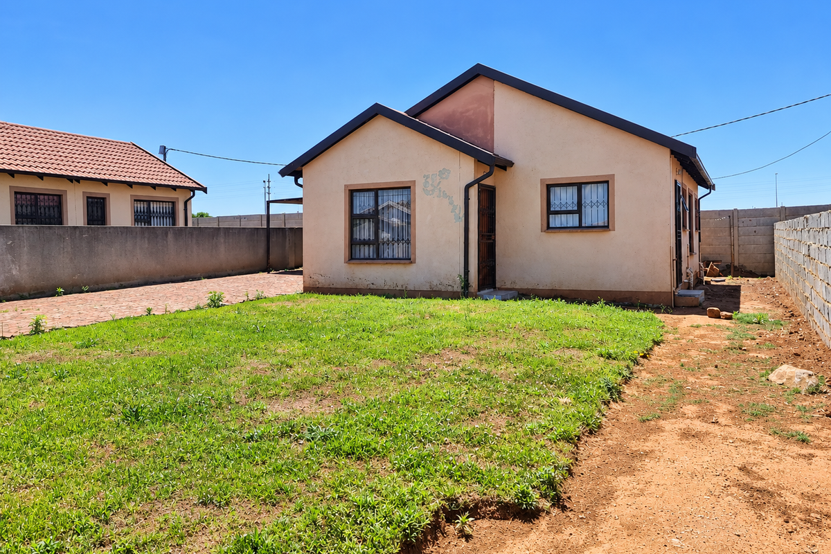 Rear view of a detached house featuring a tiled roof, security bars on windows, and a private garden area with perimeter walling.